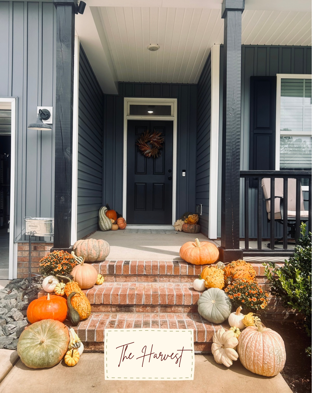 Pumpkins and mums lining the steps of a dark blue front porch